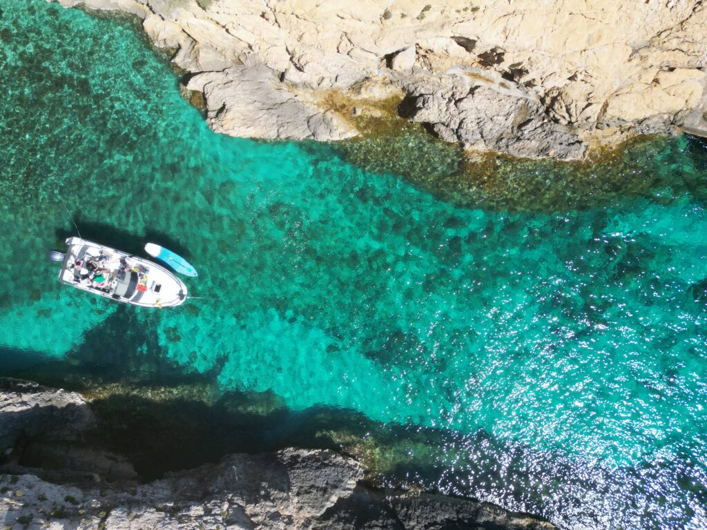 Gozo boat tour with guests swimming off the boat in clear blue water, enjoying calm conditions along the island’s coastline.