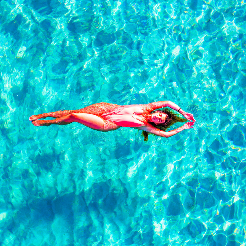 Lady floating in crystal blue water at the Blue Lagoon, Malta, wearing a pink bikini with no people, reached by private boat.