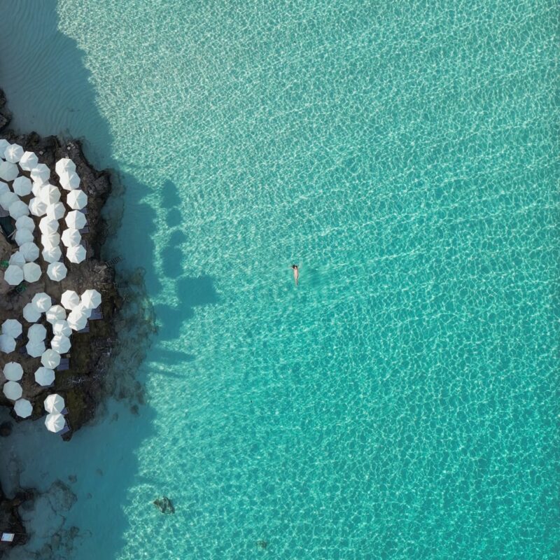 Aerial photo of Blue Lagoon Malta showing blue water, umbrellas and deckchairs from above in summer.