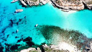 Blue Lagoon Comino with crystal clear blue water seen from boat, showing shallow turquoise sea and white limestone surroundings.