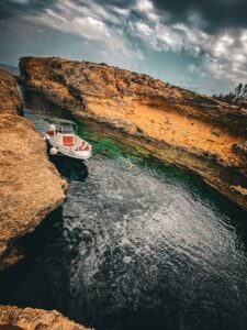 Boat cruising through the Comino gorge near San Niklaw Bay, Malta, surrounded by clear blue water and rugged limestone cliffs.