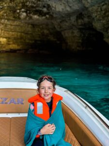 Family with a child wearing a life jacket on a boat tour in Malta, exploring a sea cave safely on calm blue water.