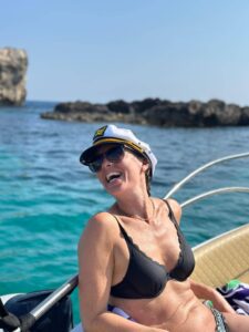 Happy lady wearing a captain hat on a private boat at the Blue Lagoon in Comino, Malta, surrounded by calm crystal blue water.