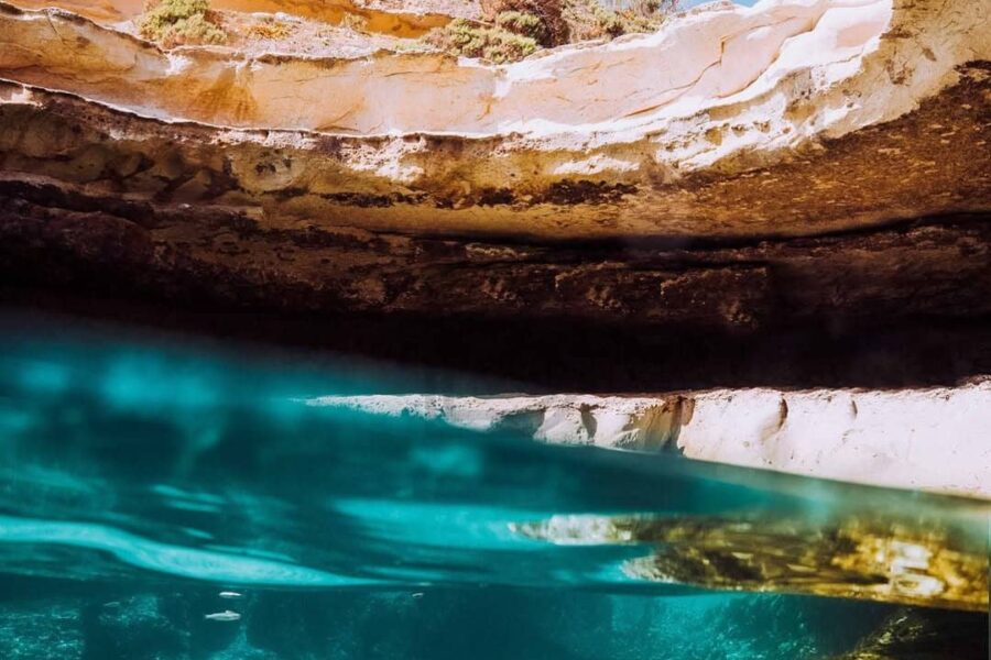 A man mid-air leaping into the deep, crystal-clear turquoise waters of St.Peter's Pool natural pool in southern Malta during a private boat tour.